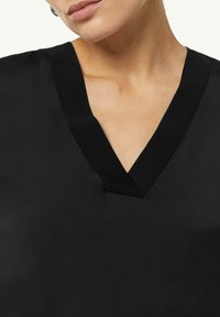 Schwarzes Oberteil mit V-Ausschnitt, aus strukturiertem Stoff und einem kontrastierenden Strickkragen. Nahaufnahme des Ausschnittdetails.