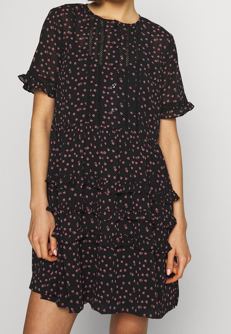 Czarna sukienka w kwiaty z falbaną na dole, krótkimi rękawami, koronkowymi detalami oraz warstwowym krojem ozdobionym małymi różowymi kwiatami.