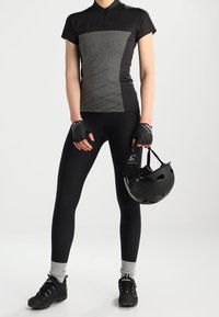 Černý a šedý cyklistický dres s krátkými rukávy, doplněný černými legínami. Součástí jsou také bezprsté rukavice a černá cyklistická přilba.