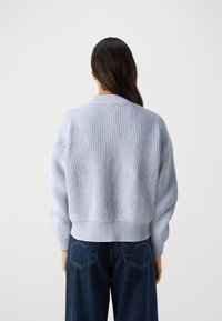 Maglione azzurro chiaro lavorato a maglia con texture a coste, spalle scese e vestibilità corta. Finitura con bordo ampio a coste. Jeans in denim visibili.