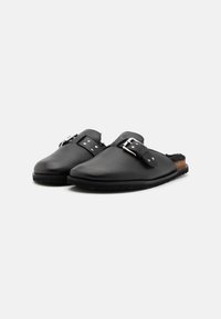 Chaussures noires en cuir à enfiler avec un bout arrondi, une sangle à boucle réglable, des clous argentés et une semelle en liège texturé.
