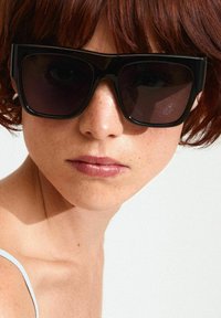Black oversized sunglasses feature a rectangular shape, dark lenses, and thick frames. The background is a plain light color, highlighting the glasses.