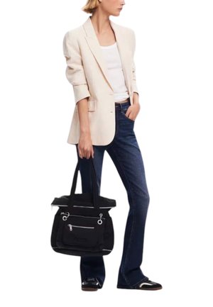 Woman wearing beige blazer, white top, blue jeans, and black sneakers, holding a black tote bag in her left hand.