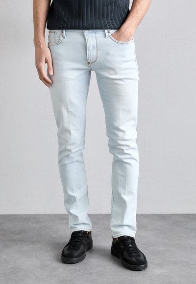 Helle blaue Jeans im Slim-Fit, mit subtilen Waschungen, fünf Taschen und genähten Akzenten, kombiniert mit schwarzen Turnschuhen.