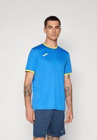 Blue athletic t-shirt with yellow collar, featuring short sleeves and a logo. Paired with dark blue shorts, made of breathable material.