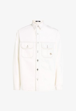 Camisa de mezclilla blanca con mangas largas, dos bolsillos en el pecho y cierres de botón plateados. Presenta costuras en contraste y un detalle con logo en el bolsillo.