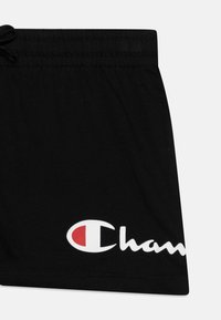 Shorts de bain noirs avec un cordon de serrage à la taille. Présentent un grand logo blanc et rouge sur le bas à l'avant. Fabriqués en tissu doux et léger.