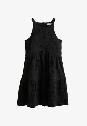 Juoda be rankovių suknelė su tekstūruota medžiaga, sluoksniuota konstrukcija ir apvalia iškirpte. Turi laisvą, pūstą siluetą.