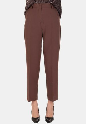 Pantaloni beige a vita alta con taglio sartoriale, bottoni frontali e tasche, indossati con tacchi a punta neri e una maglietta scura con texture.