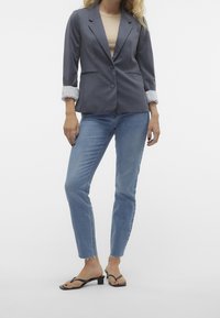 Šedý fitted blejzr se zapínáním na dva knoflíky a ohrnutými rukávy, v kombinaci s světle modrými rovnými džíny a černými sandály na podpatku.