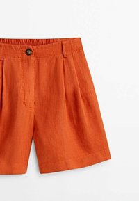 Shorts en lin orange taille haute avec plis, passants de ceinture, fermeture à bouton sur le devant et taille élastique au dos.