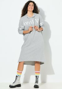 Harmaa hupullinen mekko, jossa on suuri valkoinen "Travel"-teksti, ylimitoitettu leikkaus ja sivuhalkiot. Yhdistetty mustiin taistelukengiin ja raidallisiin sukkiin.