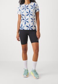 Short-sleeve athletic shirt in light blue with floral pattern, paired with black bike shorts. Shoes are light blue with orange accents.