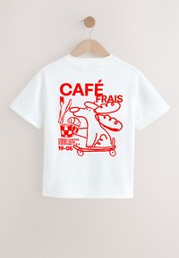 T-shirt blanc à manches courtes avec un graphisme rouge représentant un chien de dessin animé sur un skateboard tenant une tasse de café, du pain et des couverts.