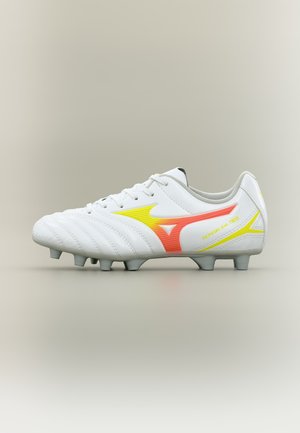 Chaussure de football blanche avec un logo orange et jaune et des crampons sous la semelle, vue de côté.