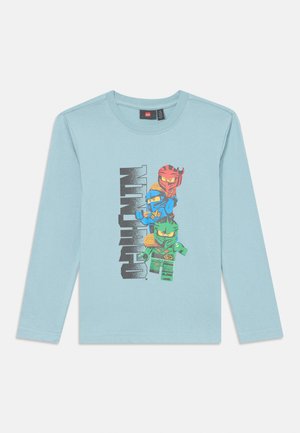 Ανοιχτό μπλε μακρυμάνικη μπλούζα με γραφικό τύπωμα τριών χαρακτήρων σε ζωντανά χρώματα, με μαύρο κείμενο που λέει "NINJAGO." Μαλακό βαμβακερό υλικό.