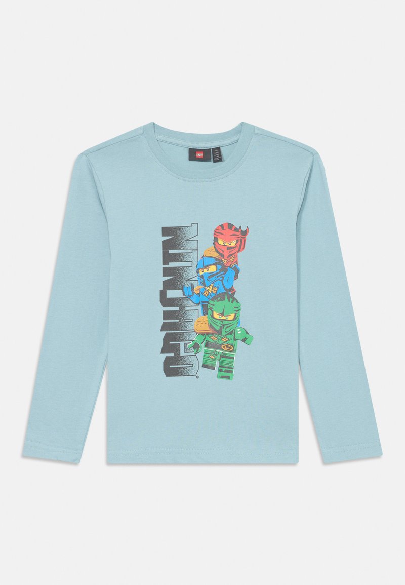Šviesiai mėlynas ilgomis rankovėmis marškinėliai su grafiniu spaudiniu, kuriame pavaizduoti trys personažai ryškiomis spalvomis, o juodu tekstu užrašyta "NINJAGO." Minkšta medvilnė.