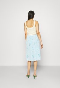 Cream ribbed cropped tank top, blue pleated midi skirt with floral print, and green high-heeled shoes, viewed from the back.