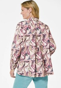 Floral-patterned blouse in pastel pink with purple and green accents, featuring a high collar and loose fit, paired with teal pants.
