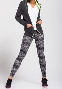 Sudadera gris con cremallera y detalles verdes, camiseta blanca, mallas negras y blancas con estampado, y zapatos negros con suelas rosas.