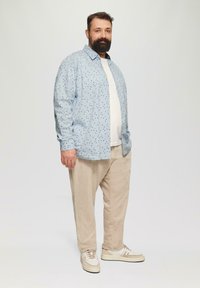 Lichtblauw overhemd met donkerblauwe stippen, witte T-shirt eronder, beige corduroy broek en crèmekleurige sneakers met accenten.