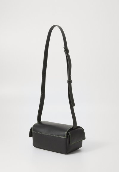 Čierna kožená crossbody taška so štruktúrovaným tvarom, zeleným prešívaním a nastaviteľným popruhom. Obsahuje klapku na uzavretie a minimálne kovové detaily.