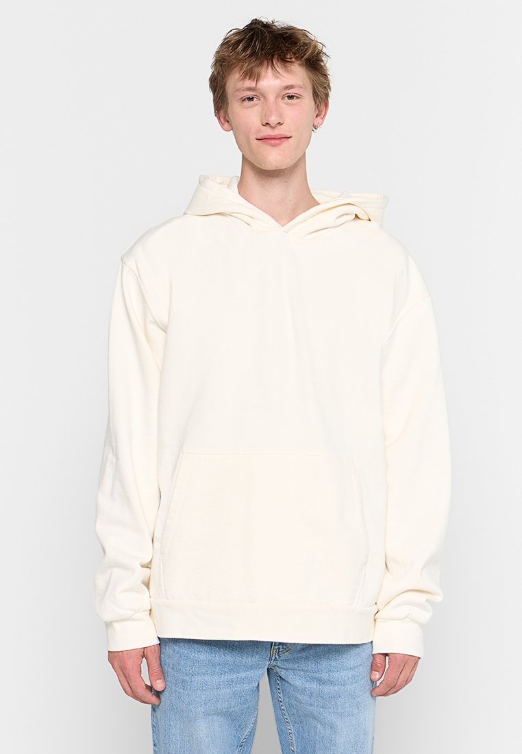 Weißer Kapuzenpulli mit Kängurutasche, lockerer Passform und gerippten Bündchen. Kombiniert mit hellblauen Jeans. Einfaches, schmuckloses Design.