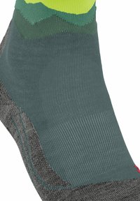 Calcetín deportivo gris con textura acanalada. Presenta un diseño en bloques de color verde y amarillo en la parte superior. Acentuado con un pequeño logotipo rojo.