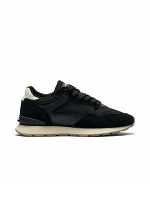 Zwarte lage sneaker met gestructureerde panelen, zwarte veters, wit hiel-detail en beige rubberen zool op een effen witte achtergrond.