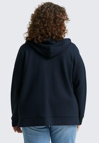 Sudadera con capucha de color marino, con cordón, textura suave y corte relajado, combinada con jeans de color azul claro.