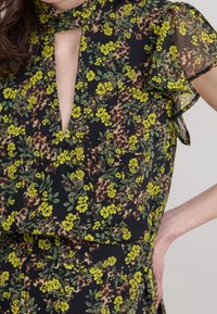 Vestido floral con un fondo negro, flores amarillas y hojas verdes, mangas cortas transparentes y un detalle de ojal en el frente.