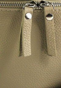 Beige leren handtas met een gestructureerd oppervlak, voorzien van zilverkleurige hardware, dubbele ritssluitingen en accentriemen bovenop.