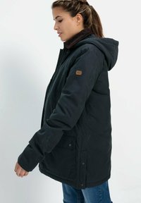 Navyblauwe geïsoleerde jas met capuchon, voorzien van een corduroy kraag en zijzakken. Effen structuur met een logo patch op de mouw.