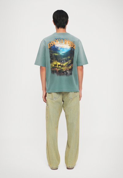 Tricou verde supradimensionat cu un imprimeu grafic de natură pe spate. Asortat cu pantaloni galbeni deschis, cu un croi lejer și buzunare tip cargo.