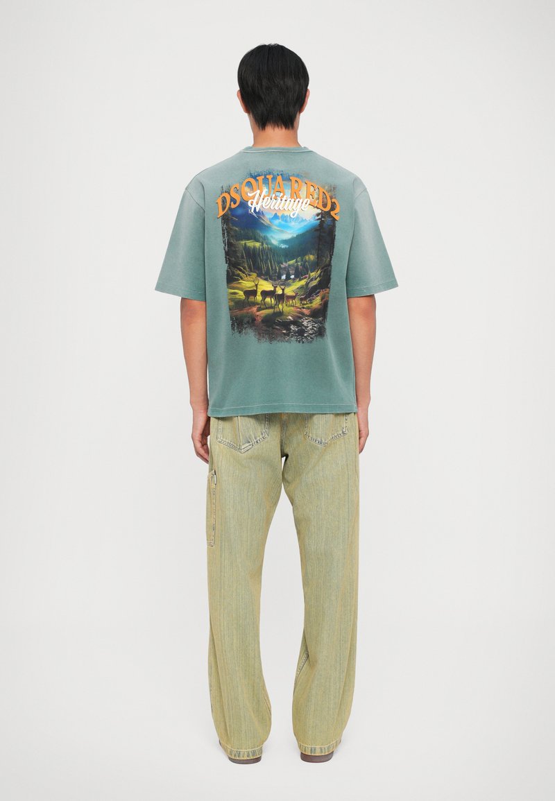 Groene oversized t-shirt met een natuurafbeelding op de achterkant. Gecombineerd met lichtgele broek met een relaxte pasvorm en cargozakken.
