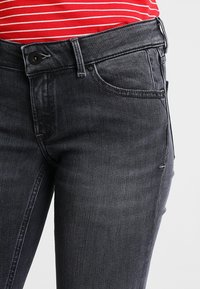 Vaqueros gris oscuro de mezclilla con un diseño clásico de cinco bolsillos, que cuentan con cierre de botón y cremallera, y un desvanecimiento sutil a lo largo de las piernas.