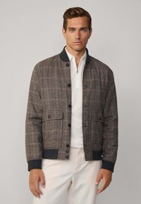 Chaqueta bomber de cuadros para hombre en tonos marrones y grises, con cuello y puños de punto, cierre de botones y dos bolsillos frontales con solapa.