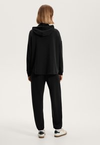 Set di felpa nera con cappuccio e pantaloni della tuta, vestibilità rilassata, texture morbida, polsini e orlo a coste, con tasca a marsupio e cappuccio piegato.