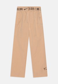 Béžové kalhoty Nike s elastickým pasem, s logem a páskem, volný střih a dvě boční kapsy. Hladká textura a rovný střih nohou.