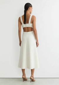 Valkoinen midi-mekko, jossa on paksut olkaimet, avonainen selkä ja vyötärö, joka kapenee ja levenee liehuvaksi hameeksi. Yhdistä vaaleanruskeiden korkokenkien kanssa.