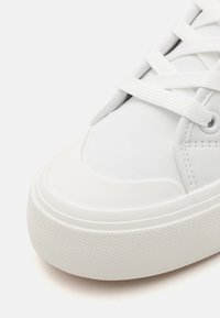 Sneaker bianchi con tomaia sintetica liscia, punta arrotondata, suola in gomma testurizzata e lacci piatti. Presenta cuciture sottili e un design minimale.