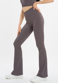 Hoog getailleerde, uitlopende leggings van een getextureerde, ribbelstof, in een gedempte grijstint. Gecombineerd met witte sportschoenen.