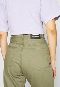 Pantaloni verde oliva a vita alta, con etichetta nera "DRDENIM", due tasche posteriori e dettagli di cucitura in evidenza.
