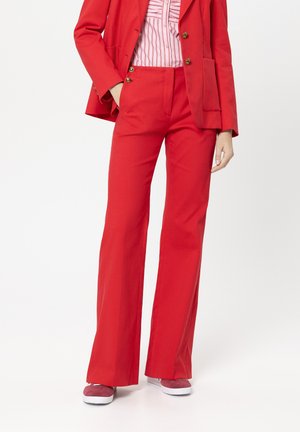 Rotes, maßgeschneidertes Blazer- und Hosen-Set mit goldenen Knöpfen, schmalem Schnitt und ausgestelltem Bein-Design, kombiniert mit pinken Schuhen und einem gestreiften Hemd.