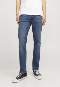 Jeans de mezclilla azul con corte recto, que presentan un ligero desgaste, diseño de cinco bolsillos y cierre de botón, combinados con zapatillas negras.