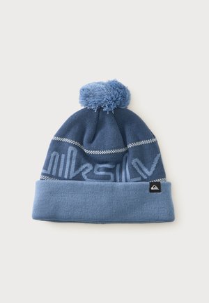 Bonnet d’hiver tricoté bleu avec pompon, revers plié et motif subtil de texte de marque, avec une petite étiquette noire de logo sur le revers.
