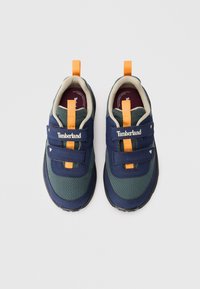 Pár modrých a zelených sieťových tenisiek Timberland s oranžovými pútkami a suchým zipsom na bielom pozadí.