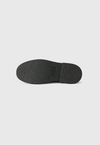 Μαύρη υφασμένη σόλα παπουτσιού με επίπεδη, στρογγυλεμένη μορφή και λεία άκρη. Περιέχει λεπτομέρεια με το λογότυπο στην περιοχή της ενδιάμεσης σόλας.