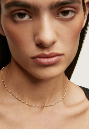 Collar choker de oro con pequeñas cuentas redondas y delicados eslabones. Textura suave, diseñado para ajustarse de cerca alrededor del cuello.