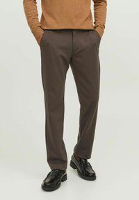 Pantalones marrones a medida con una textura suave y un diseño clásico. Presenta bolsillos laterales y un corte de pierna recta. Llevado con mocasines negros.